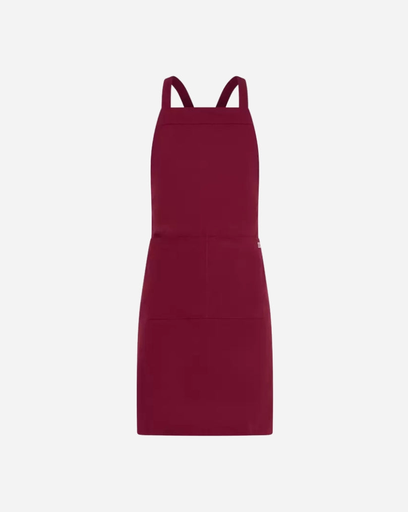 Grembiule unisex bordeaux in poliestere e cotone con pettorina, tasca centrale e allacciatura con bretelle regolabili tramite anello in ottone.