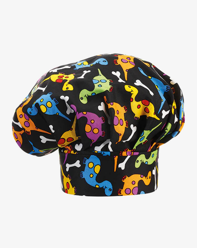 Cappello da cuoco nero in misto cotone con vivace fantasia multicolore a tema dinosauri stilizzati e piccoli ossi bianchi, fascia piatta regolabile con velcro e parte superiore a sbuffo.

