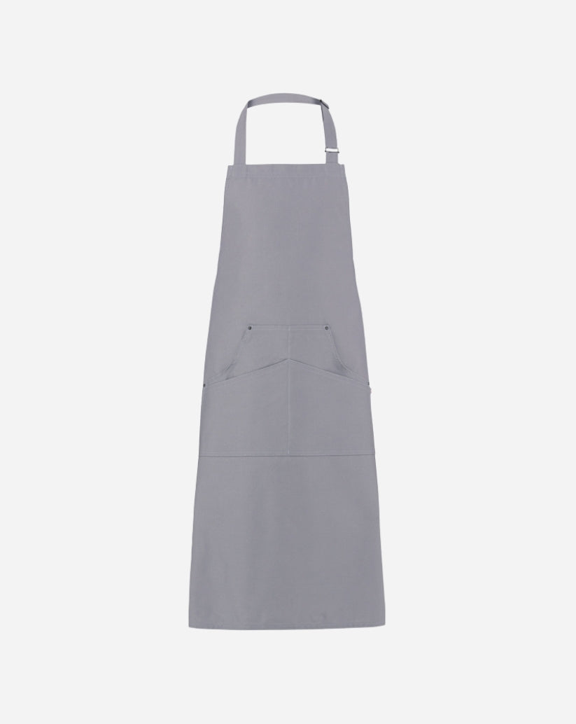 Grembiule a pettorina grigio in twill di cotone con fibbia regolabile in ottone, tasca centrale e rivetti antichi.