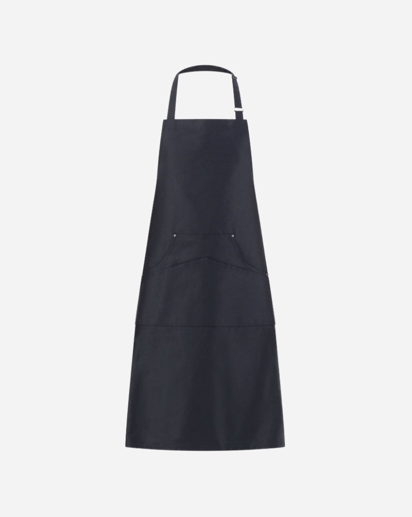 Grembiule a pettorina nero in twill di cotone con fibbia regolabile in ottone, tasca centrale e rivetti antichi.